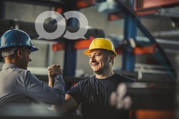 Two construction workers wearing hard hats shake hands and are happy about their successful collaboration.