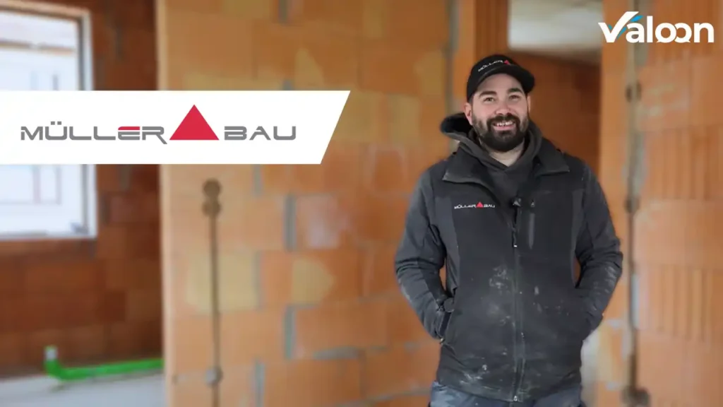 Mitarbeiter von Müller Bau steht lächelnd auf einer Baustelle mit Valoon-Logo im Bild